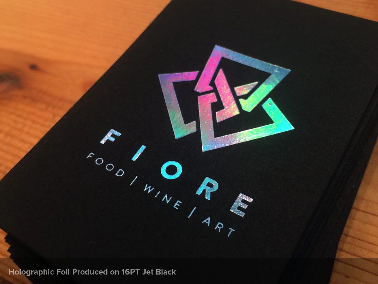 A close-up of a business card featuring a holographic foil logo on a black background, with the text "FIORE FOOD | WINE | ART."